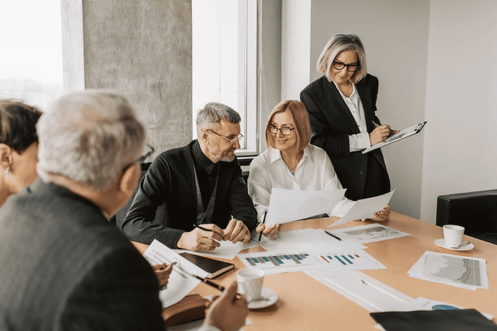 How Much Does it Cost to Maintain A Website Monthly? 3 A group of business people sitting around a table in a meeting, discussing the monthly cost of maintaining a website.