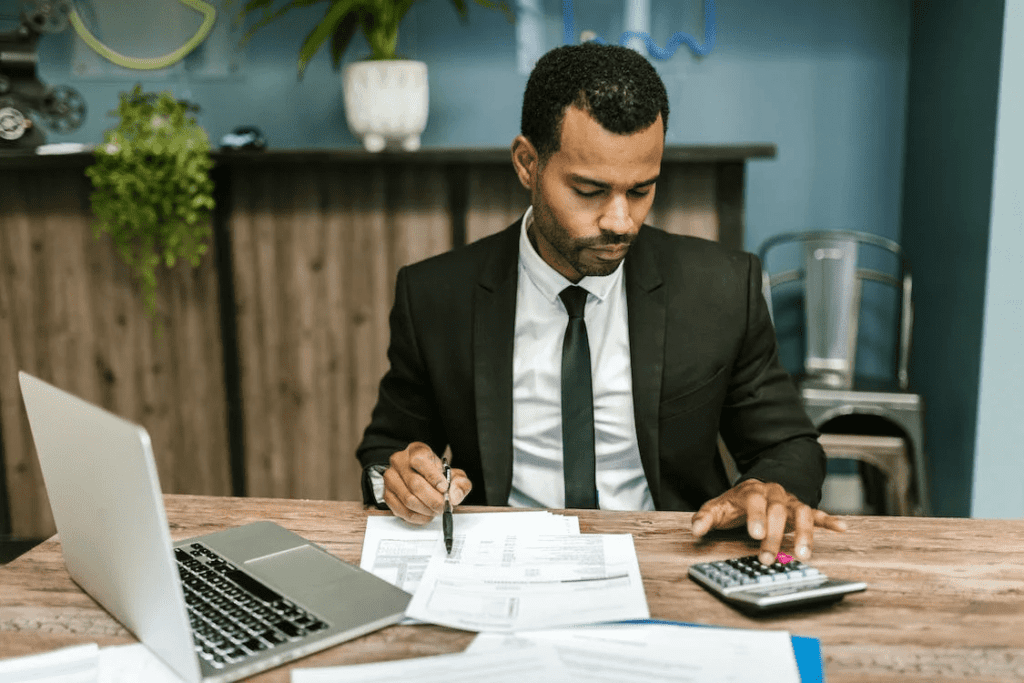 How Much Does it Cost to Maintain A Website Monthly? 4 A man in a suit sitting at a desk with paperwork and calculating the monthly maintenance cost of a website.